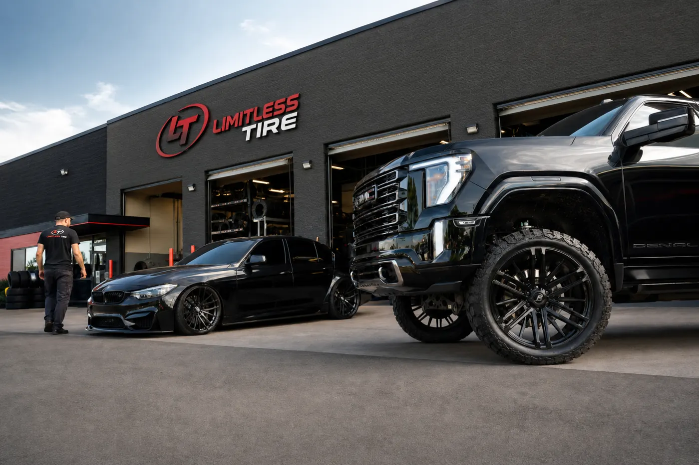 Lifted truck with aftermarket wheels and all-terrain tires next to a lowered sports car with dark window tint at a Limitless Tire shop